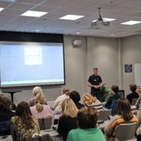 Male eye-share employee presenting something on a big screen in front of seated audience